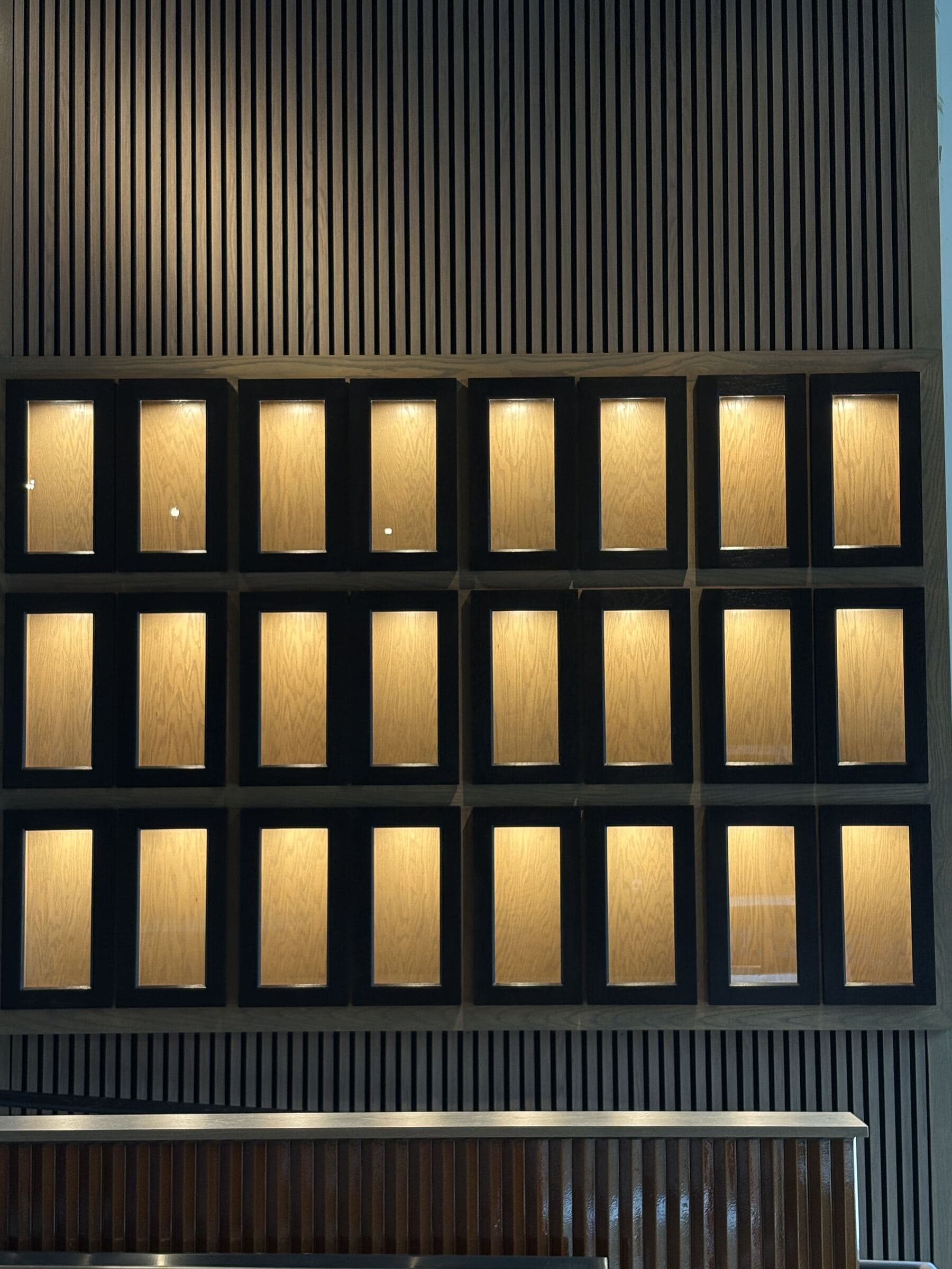 Wall of backlit oak tequila lockers with black frames at La Victoria